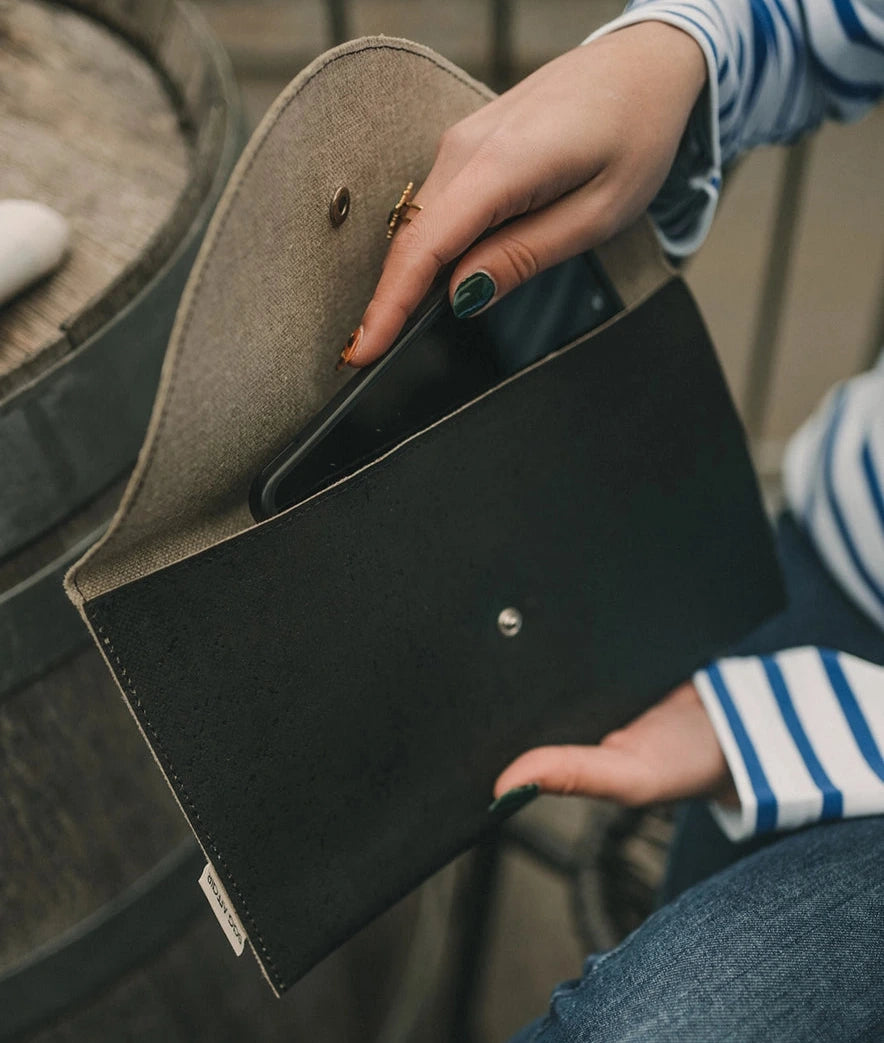 Musta kirjekuorilaukku ja puhelin mallin käsissä